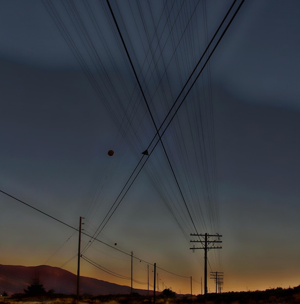 Photo low angle view of silhouette electricity pylons against sky at dusk