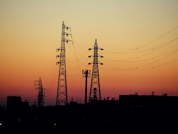low angle view of silhouette electricity pylons at sunset