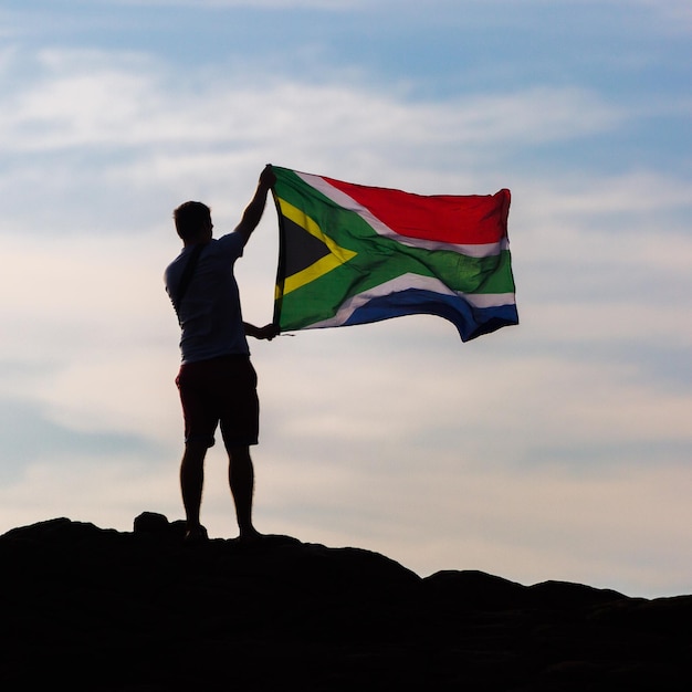 Photo low angle view of silhouette man holding south african flag standing against sky