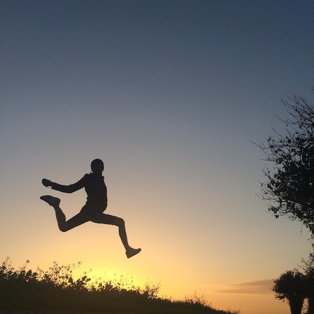 Low angle view of silhouette man jumping against clear sky