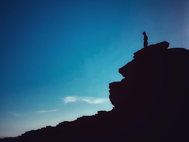 Low angle view of silhouette man on rock against blue sky