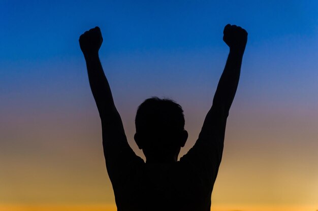 Photo low angle view of silhouette man with hand raised against sky