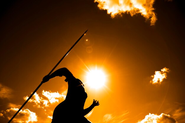 Photo low angle view of silhouette man with javelin against sky during sunset