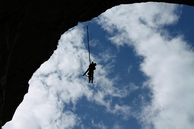 Foto vista a bassa angolazione della silhouette di persone che si arrampicano sulla scogliera contro il cielo