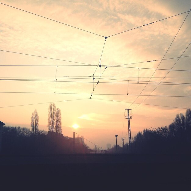 Foto vista a bassa angolazione delle linee elettriche a silhouette contro un cielo nuvoloso durante l'alba