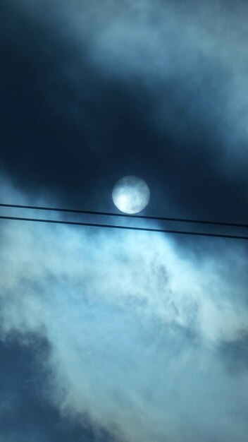 Foto vista a basso angolo delle linee elettriche a silhouette contro la luna piena in un cielo nuvoloso