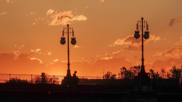 Low angle view of silhouette street lights against orange sky