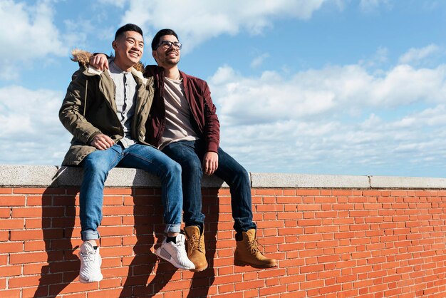 Low angle view of smiling friends sitting on brick wall