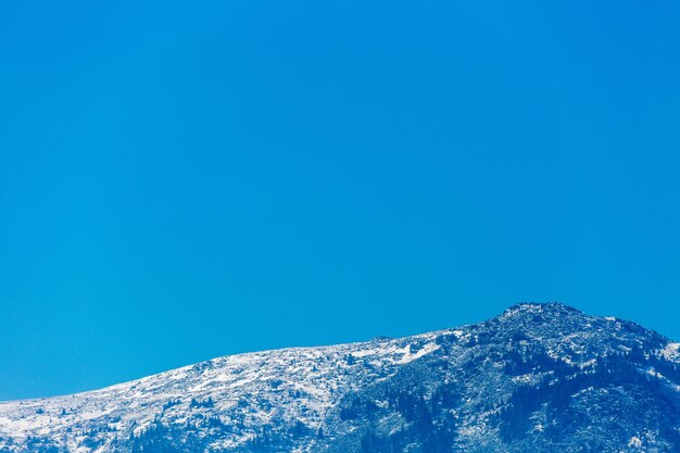 Low angle view of snowcapped mountain against clear blue sky