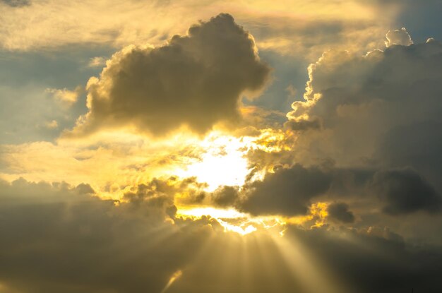 Low angle view of sunlight streaming through clouds during sunset