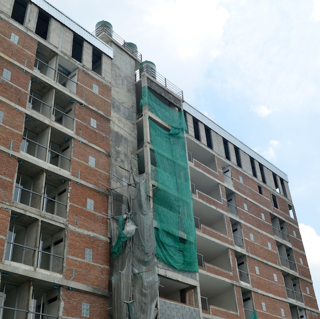 Low-angle view of a tall commercial building under construction against a blue sky