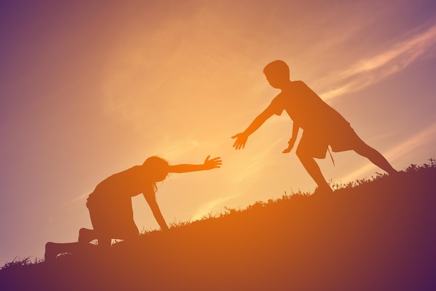 Photo low angle view of teenage boy helping girl climbing on hill against sky during sunset