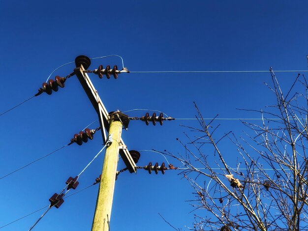 Low angle view of telephone pole against clear blue sky