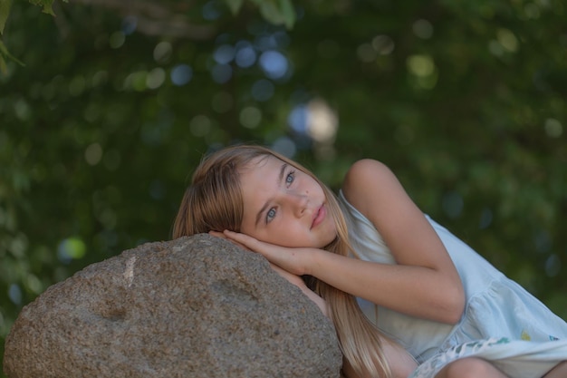 Photo low angle view of thoughtful girl looking away while lying on rock at park