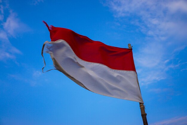 Low angle view of torn flag against blue sky