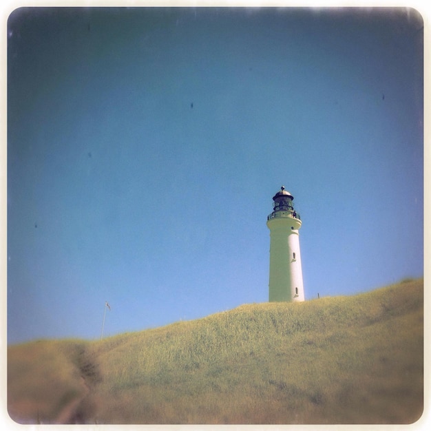 Foto vista a basso angolo del faro bianco sul campo contro un cielo limpido.