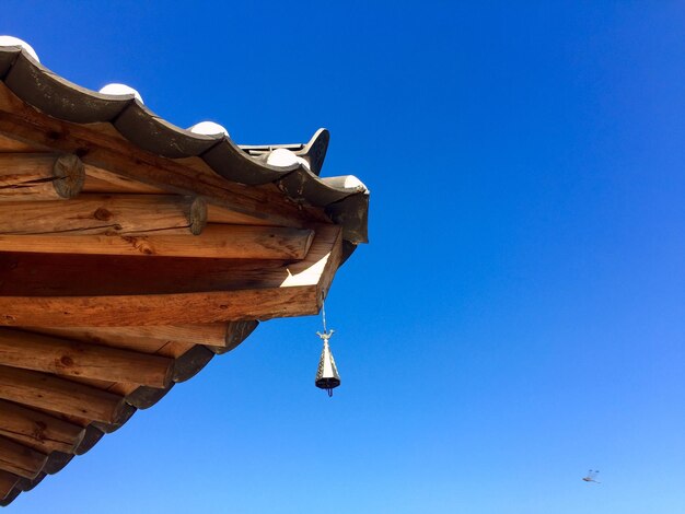 Low angle view of wind chime on roof against clear blue sky