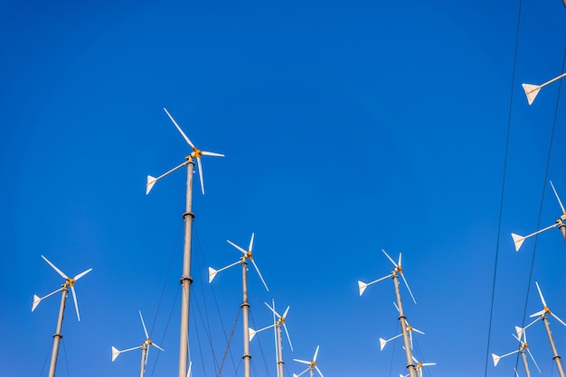 Low angle view of wind turbines against clear blue sky
