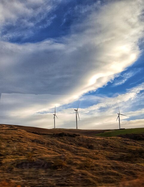 Low angle view of wind turbines on field against sky