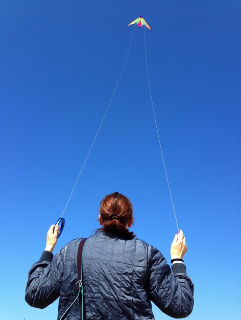 Low angle view of woman flying against clear blue sky