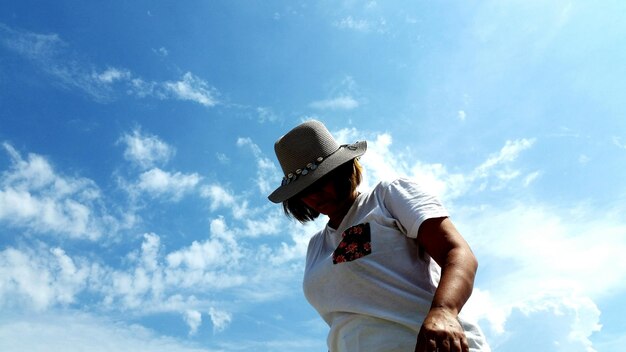 Low angle view of woman in hat standing against sky