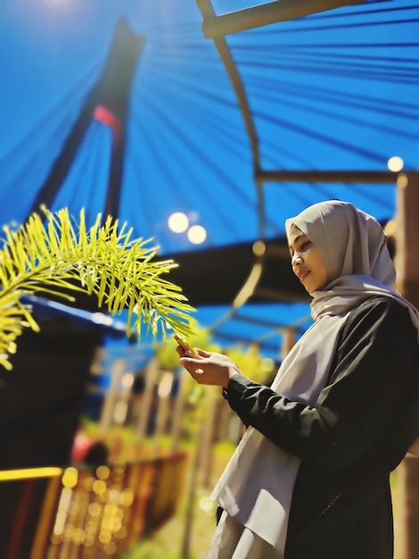Photo low angle view of woman in hijab touching plant outdoors