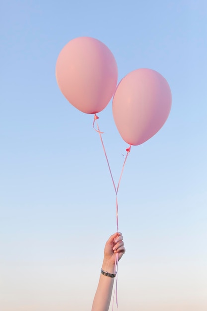 空にピンクのヘリウム気球を抱えている女性の低角度の視点