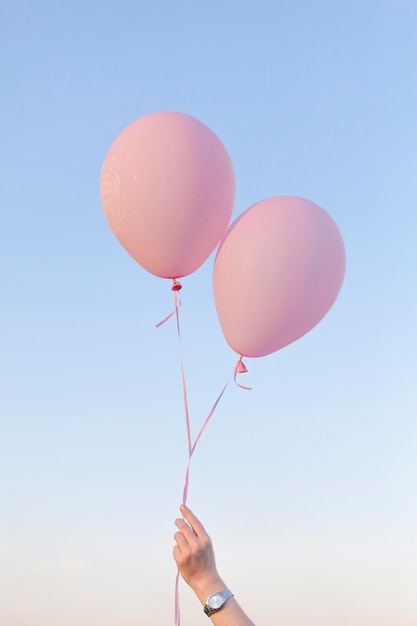 空に向かってピンクのヘリウム風船を握っている女性の低角度の写真