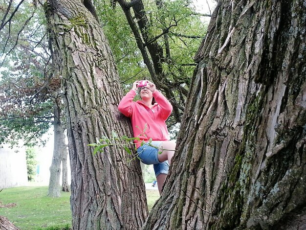 Low angle view of woman leaning on tree while photographing