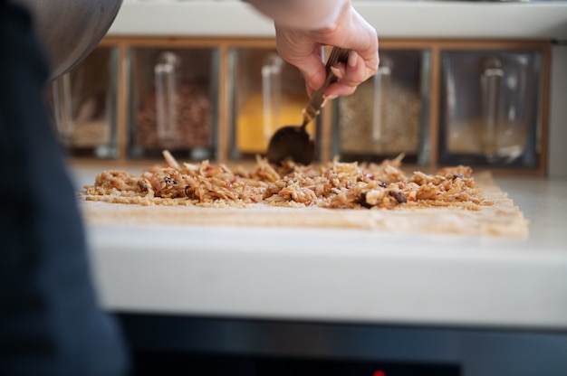 Inquadratura dal basso di una donna che prepara uno strudel di mele disponendo il ripieno sull'impasto sul bancone della cucina.