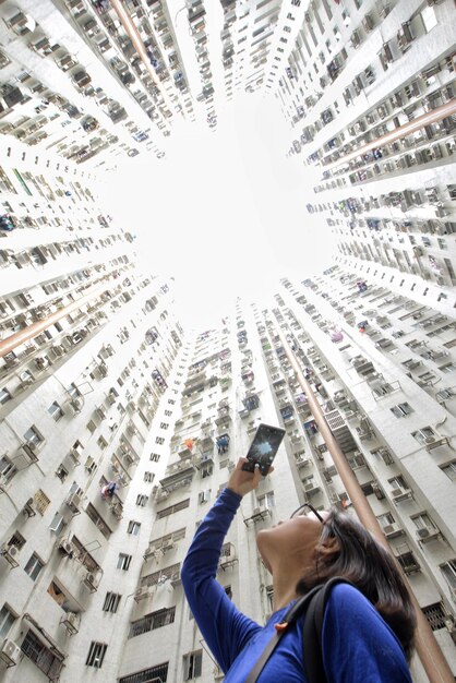 Foto vista ad angolo basso di una donna che scatta foto con il telefono cellulare vicino agli edifici della città