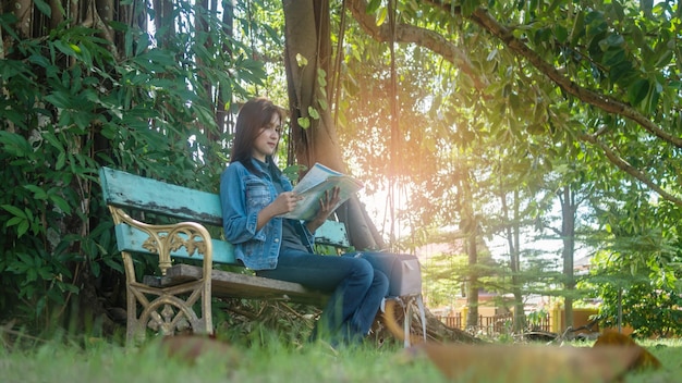 Low angle view of woman reading map while sitting on bench at park