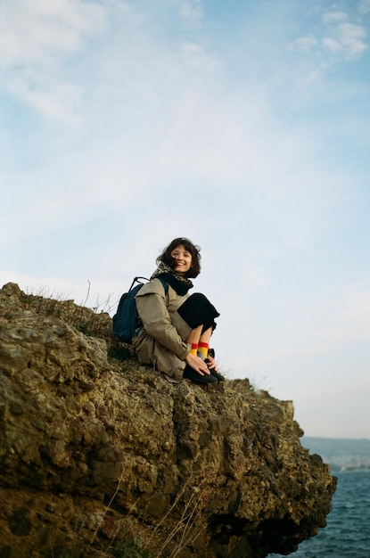空の向こうの岩の上に座っている女性の低角度の写真