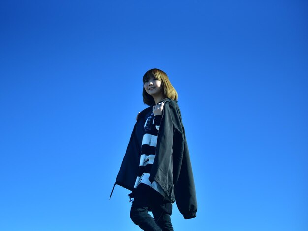 Low angle view of woman standing against clear blue sky