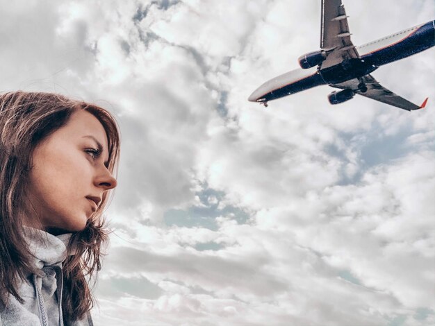 空を飛ぶ飛行機の前に立っている女性の低角度の景色