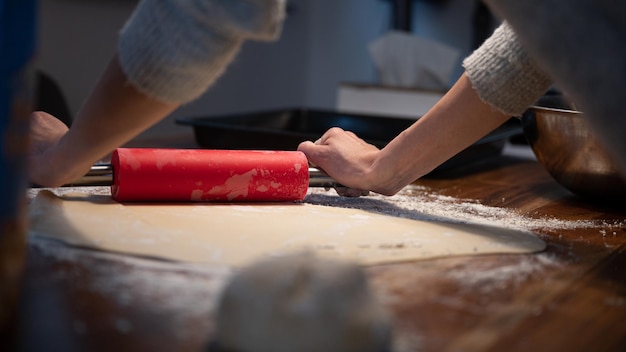 Inquadratura dal basso di una donna che usa il mattarello per arrotolare la pasta sfoglia fatta in casa