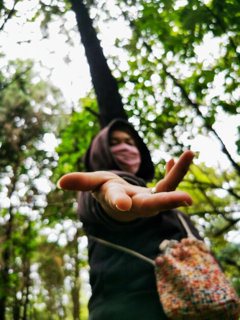 Foto vista a basso angolo di una donna che indossa una maschera in piedi nella foresta