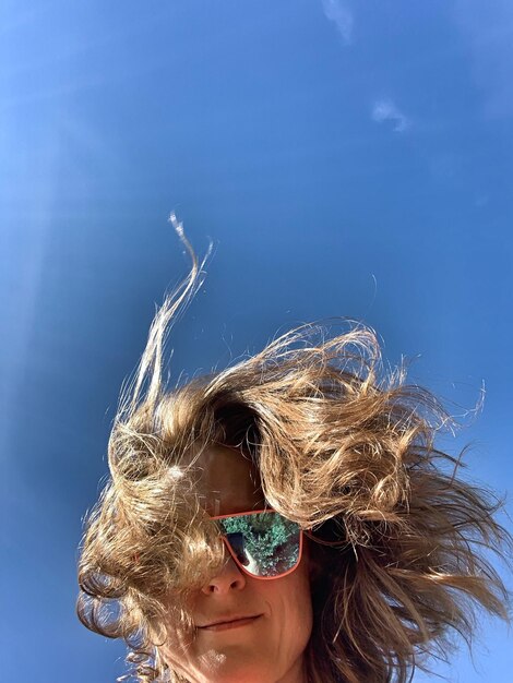 Foto vista a basso angolo di una donna con i capelli lunghi che indossa occhiali da sole contro un cielo blu limpido