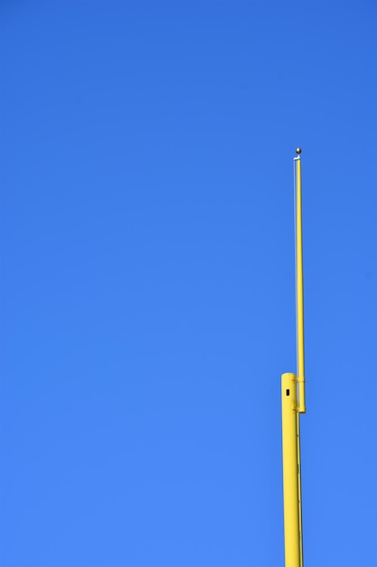 Low angle view of yellow pole against clear blue sky
