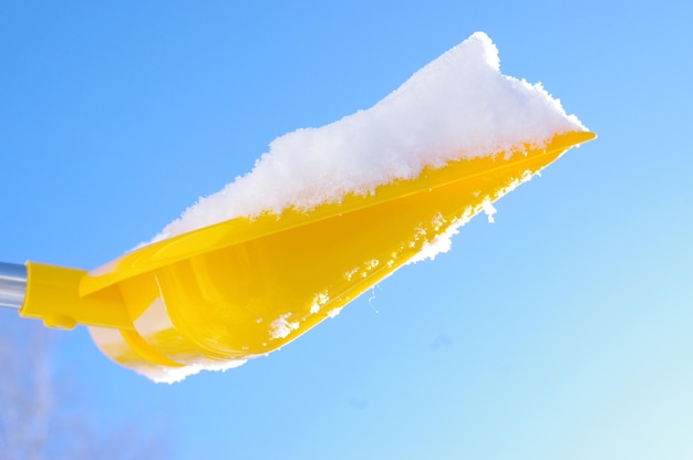 Low angle view of yellow shovel with snow against clear blue sky