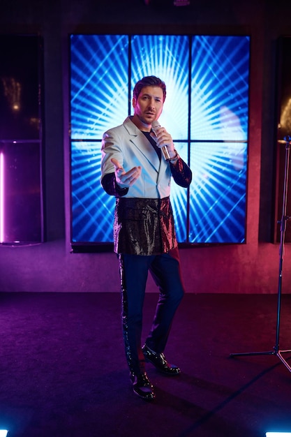 Photo low angle view of young male singer holding microphone standing and performing on stage in music club