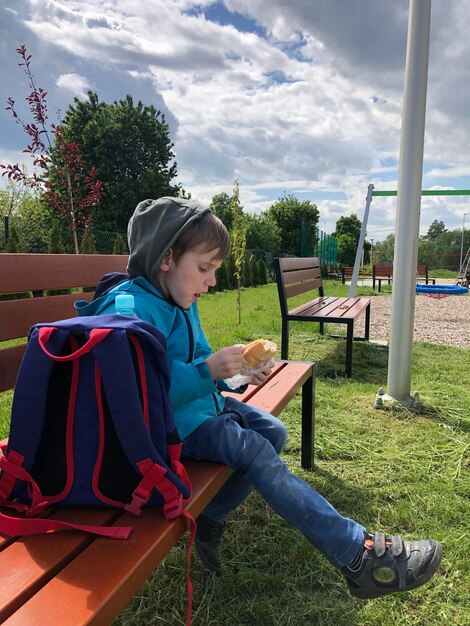 Low angle view of young man sitting on the bench against sky