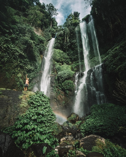 Foto vista ad angolo basso di un giovane in piedi contro una cascata nella foresta