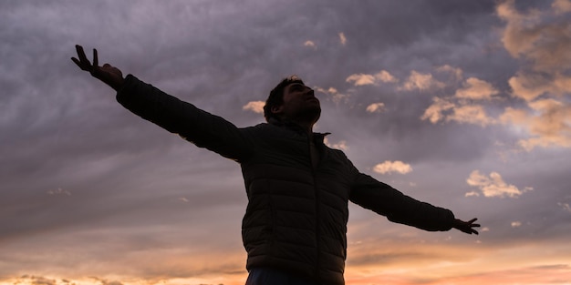 輝く夕方の空の下に立っている若い男のローアングルビュー