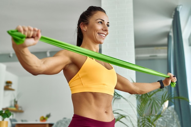 Low angle view of young muscular build woman exercising with resistance band in the living room