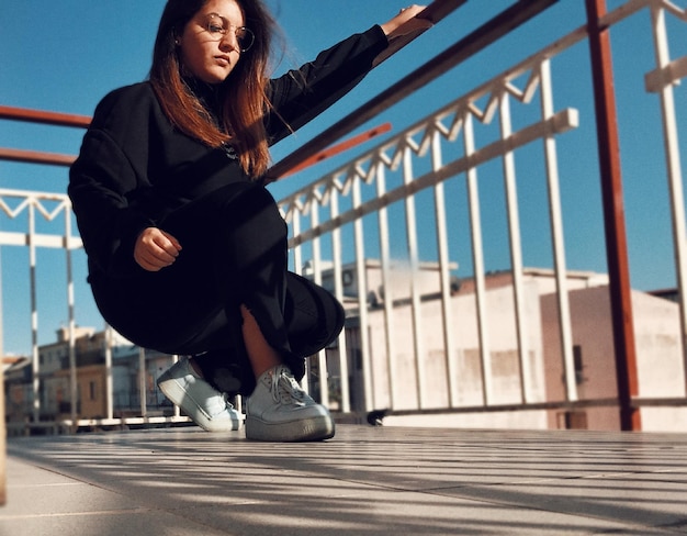 Photo low angle view of young woman crouching against railing