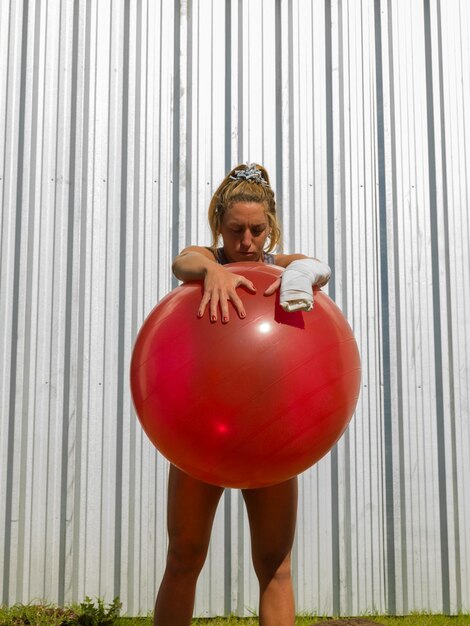 Low angle view of young woman holding fitness ball while standing against wall
