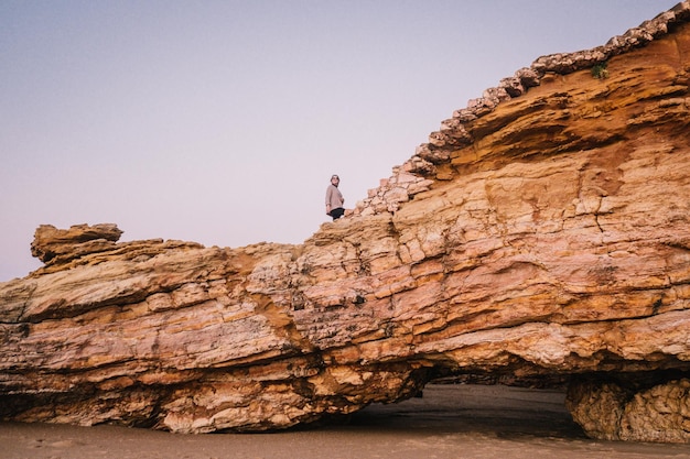 Photo low angle view of young woman standing on cliff against clear sky