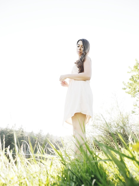 Photo low angle view of young woman standing on grassy field against clear sky