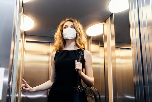 Foto vista a basso angolo di una giovane donna che indossa una maschera nell'ascensore